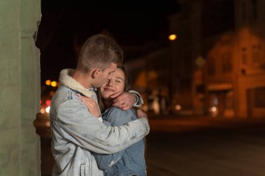 Adam şefkatle sarılıp kız arkadaşını öpüyor. Mutlu genç çift sarılıyor, akşam kenti geçmişi. Sokakta romantik bir randevu..