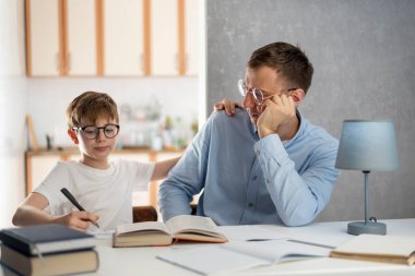 Baba ve oğul birlikte ödev yapıyorlar. Evde eğitim. Genç çocuk evde çalışıyor. Babam ve okul çocuğu ödev yapıyor.