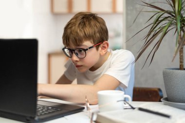 Ergen çocuk programcılıkla meşgul. Gözlüklü çocuk dikkatle laptop monitörüne bakıyor. Ev okulu .