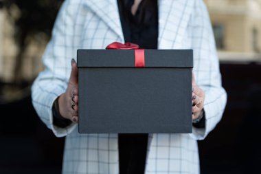 Kadının elindeki siyah hediye kutusunun fotoğrafını kapat. Elinde güzel bir hediye kutusu tutan bir kız. Boşluğu kopyala.