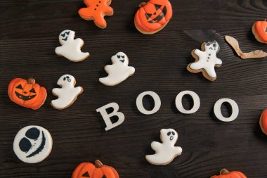 Kahverengi ahşap bir masaya yerleştirilmiş balkabağı, gülen hayalet şeklinde turuncu ve beyaz kurabiyelerden oluşan Cadılar Bayramı dekoru. Yazı Booo.