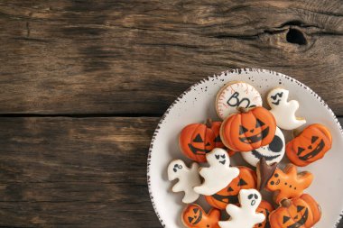 Cadılar Bayramı için hazırlık. Beyaz bir tabak turuncu ve beyaz zencefilli bisküvi kahverengi ahşap bir masada duruyor. Metin için boşluk.