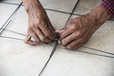 İnşaat işçisi yapısal çeliği bağlıyor, zemin beton dökümü hazırlanıyor.