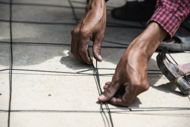 İnşaat işçisi yapısal çeliği bağlıyor, zemin beton dökümü hazırlanıyor.