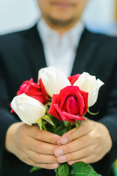 A man is giving white and red rose bouquet. Photo is focused at the middle red rose.