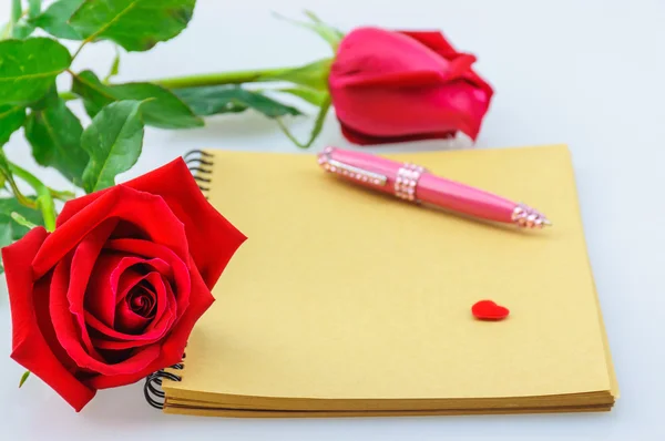 Red rose and pink pen with notebook. Photo is focused at the left rose. — Stock Photo, Image