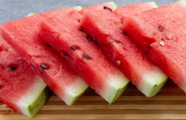 Ahşap bambu tahtasının üzerinde üçgen şeklinde kırmızı karpuz dilimleri var.