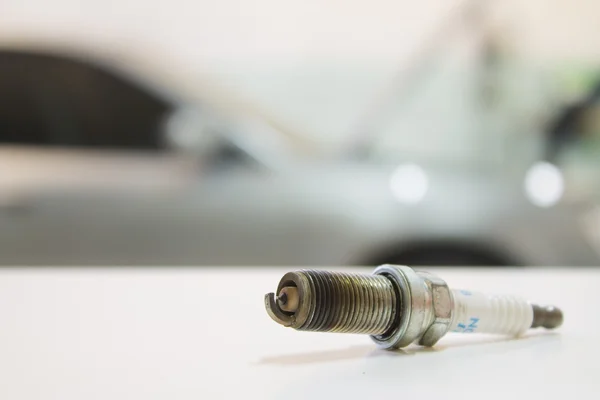 Bujía usada disparo primer plano en una mesa blanca contra el coche — Foto de Stock