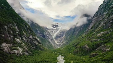 Kayaların arasında güzel bir vadi, arka planda bir dağ beyaz, aşağıda bir nehir akıyor, bulutlar.