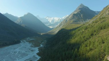 Yandan güneş ışığı parlıyor ve dağları ve vadiyi sular altında bırakıyor.