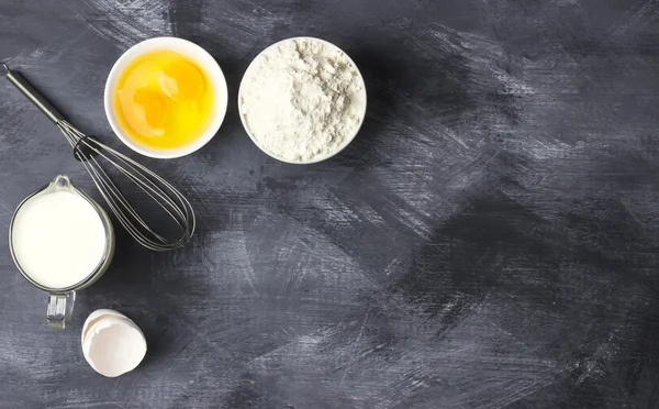 Ingredients for pastries: flour, eggs, milk against a dark backg