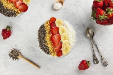 Sağlıklı kahvaltı güler yüzlü chia, coco, çilek, fındık ve muz üzerinde beyaz bir arka plan ile. Üstten Görünüm