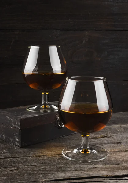 Conhaque em dois copos em um fundo de madeira escura — Fotografia de Stock