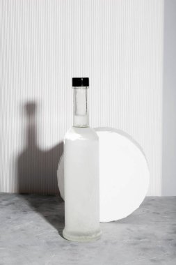 Bir şişe votka ve beyaz stand. Gölgeler ve güneş ışığı eğilimleri