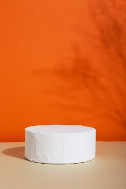 Paketleme sunumu için podyum ve kozmetik, duvarda gölge. Beyaz beton desenli ürün sergisi. Turuncu arka planda güneş ışığı altında doğal güzellik kaidesi