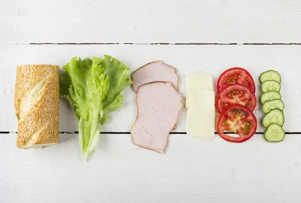 Ingredients for sandwich: lettuce, bacon, tomatoes, cucumber, cheese on a white wooden background — Stock Photo, Image