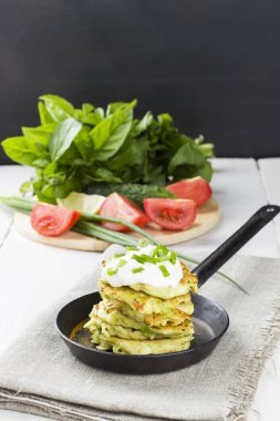 Kabak börek kızartma tavası üzerinde ekşi krema, beyaz arka plan üzerinde çeşitli sebze ile