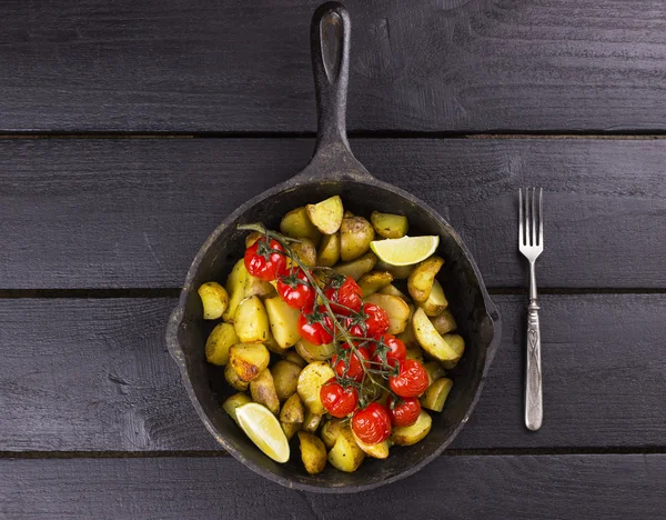 Frying pan with fried potato and the baked cherry tomatoes on br
