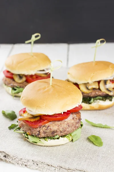 Vegetarian burger with haricot, couscous, mushrooms, arugula and tomatoes on a wooden background