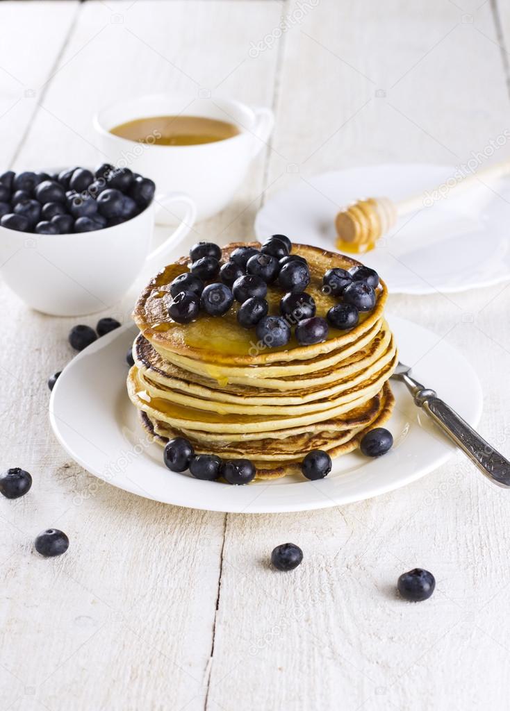 heap of pancakes watered with honey and blueberry on a white woo