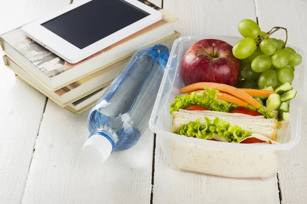 Lunchbox with sandwich, vegetables and fruit, bottle of water and pad on a white background — Stock Photo, Image