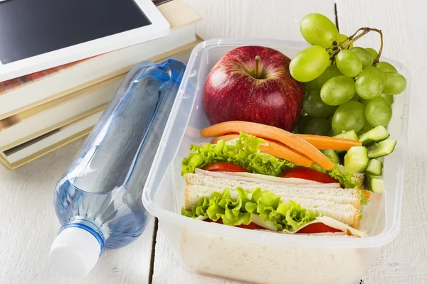 Lunchbox with sandwich, vegetables and fruit, bottle of water and pad on a white background — Stock Photo, Image