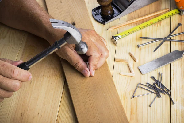 The carpenter hammers nail into a plate on the desktop with tools — Stock Photo, Image