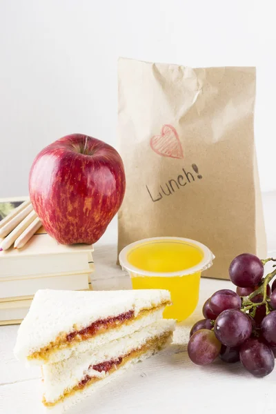 Lunchbox in school: sandwich with peanut butter and jam, apple, grapes, jelly on a white wooden background