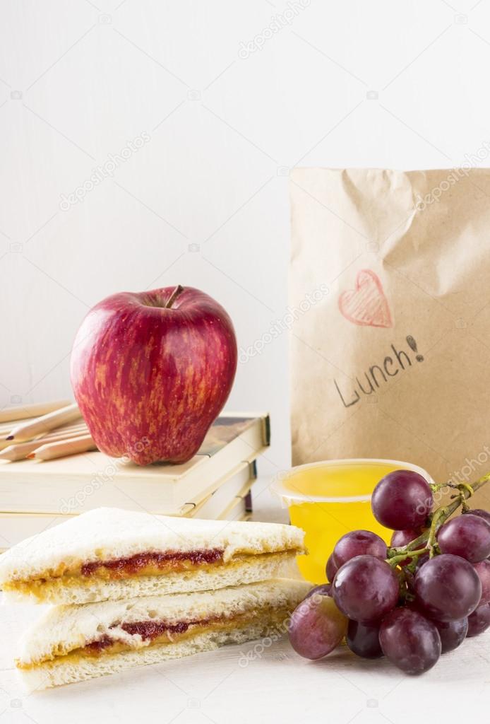 Lunchbox in school: sandwich with peanut butter and jam, apple, grapes, jelly on a white wooden background