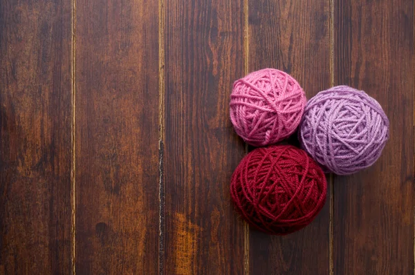 Three skeins in red and pink tones over wooden background — Stock Photo, Image