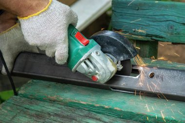 Bir çilingir, sürtünme kuvvetiyle kıvılcımlar uçuşurken ahşap bir bankta metal bir değirmenciyle testereyi testereyle keser.