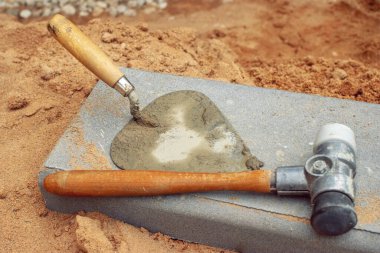 İnşaat malzemelerinin yanında duran özel çekiç ve spatula.