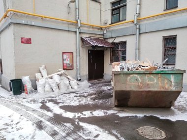 Girişe yakın büyük bir çöp tenekesi paslı retro konteynır ve inşaat torbası.