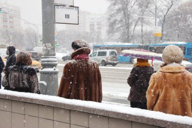 Kışın kar yağarken insanlar otobüs durağında bekliyor.