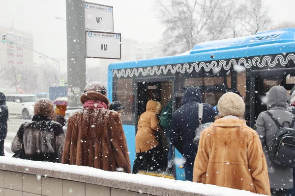 Kışın kar yağarken insanlar otobüs durağında bekliyor.