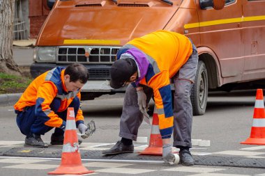 Yol işlerinin ustaları yapışkan bant ve yolda bir spatulayla çalışıyorlar.