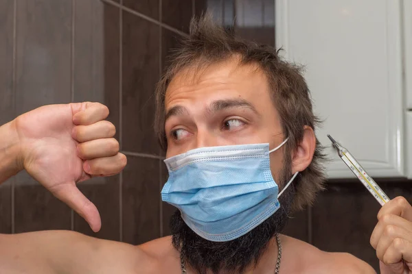 Ένας Άντρας Γενειάδα Ιατρική Μάσκα Κοιτάζει Θερμόμετρο Και Δείχνει Μια — Φωτογραφία Αρχείου
