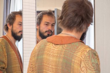 Sabahlık giymiş sakallı bir adam aynaya bakıyor. Çift yansıma.