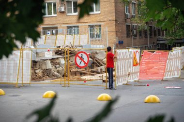 Tamirci çitin içinden geçiyor ve onu parçalara ayırıp inşaat alanına geçiyor..