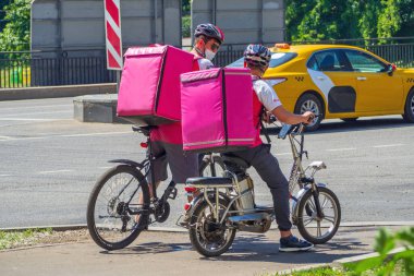 İki kurye, yemek ve günlük ürünleri sarı bir taksinin yanına getiriyor.