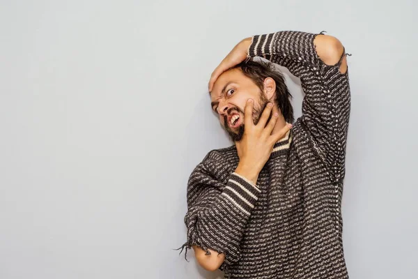 Sakallı bir adam (uçta saç), korku içinde, ahlaken kendi tarafından köşeye sıkıştırılmış. (Dirseklerinde delikler olan süveter giyen bir adam).