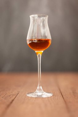 Kanyak, şeri ya da açık gri arkaplanlı ahşap masa üzerinde konyak ya da calvados içeren Grappa camı..