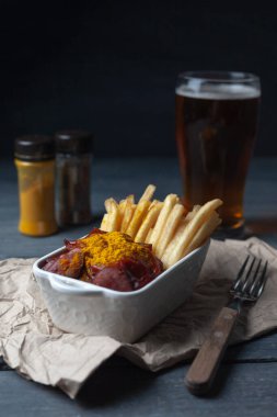 Bira ile servis edilen ahşap masadaki patates kızartmasıyla kıvırcık sosis. Dikey yönelim.