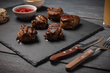 Koyu ahşap masada taş tahtada ketçaplı ızgara domuz madalyonu..