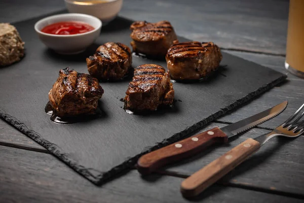 Gegrillte Schweinemedaillons mit Ketchup auf Steinplatte auf dunklem Holztisch serviert. — Stockfoto