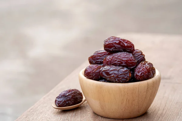 Medjool dates or dates fruit in wooden bowl and spoon on table, This fruit is highly nutritious and is commonly eaten during fasting or Ramadan.