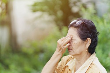 Yaşlı bir Taylandlı kadın göz çukurlarına masaj yapmak için kafasına gözlük takıyor çünkü gözlerinde ağrı var. Sağlık hizmeti kavramı.
