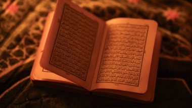 İslam kültürünü ve maneviyatını temsil eden sıcak ortam ışığı altında desenli bir kumaşa yerleştirilmiş Arapça metni olan kutsal Kur 'an' ı açın..