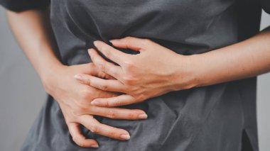 Muhtemelen hazımsızlık, kramplar ya da sağlık sorunları yüzünden karnını ağrıtan bir insanın yakın çekimi rahatsızlığı ve tıbbi kaygıları simgeliyor..