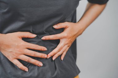 Karın ağrısı çeken bir kadın, iki eliyle karnını tutuyor, sindirim sorunları, kramplar veya mide ağrısı belirtileri gösteriyor..